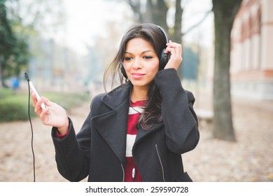 Young Beautiful Indian Woman At The Park In Autumn Listening Music With Headphones