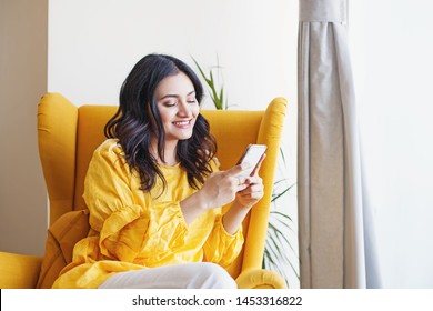 Young Beautiful Indian Woman Using Her Mobile Phone While Sitting In The Armchair At Home