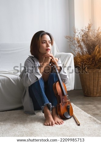 Young beautiful lady sit on the chin and holding violin,with romantic emotion,potrait model posing,blurry light around