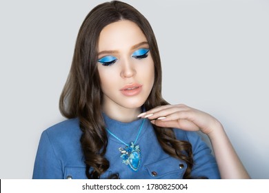 Young Beautiful Lady Wearing Blue Denim Blouse. Massive Necklace Colorful Crystals. Professional Make-up Pencil Technique Cut Crease, Beige Lips. Long Curly Hair