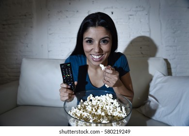 young beautiful latin woman home alone watching television smiling sitting at sofa couch on living room happy and excited enjoying TV show or movie relaxed in dark light eating popcorn - Shutterstock ID 580219249