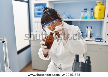 Young beautiful latin woman scientist holding plant with tweezers on bottle at laboratory
