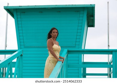 Young, beautiful Latin woman standing on the lifeguard stand on a beach in Cadiz, Spain. She looks out to sea and enjoys the view. The air is blowing and the sea breeze is blowing - Powered by Shutterstock