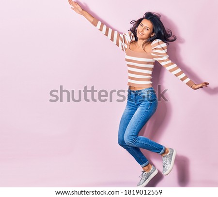 Young beautiful latin woman wearing casual clothes smiling happy. Jumping with smile on face over isolated pink background