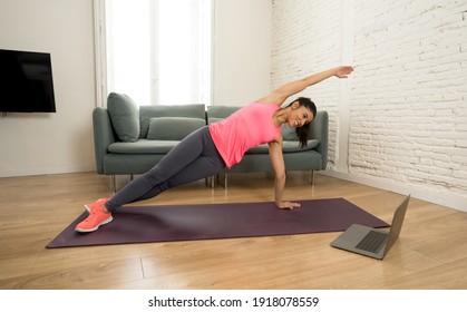 Young Beautiful Latin Woman Working Out At Home Connected To Online Fitness Class On The Computer Laptop. Woman Personal Trainer Coach On Zoom Teaching Exercises In Live Streaming Workout Class.