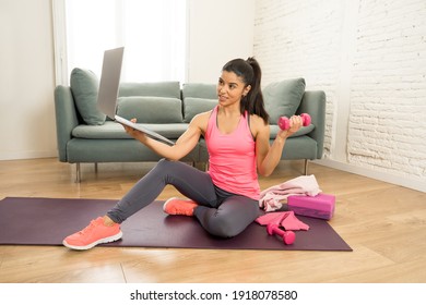 Young Beautiful Latin Woman Working Out At Home Connected To Online Fitness Class On The Computer Laptop. Woman Personal Trainer Coach On Zoom Teaching Exercises In Live Streaming Workout Class.