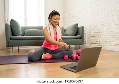 Young Beautiful Latin Woman Working Out At Home Connected To Online Fitness Class On The Computer Laptop. Woman Personal Trainer Coach On Zoom Teaching Exercises In Live Streaming Workout Class.