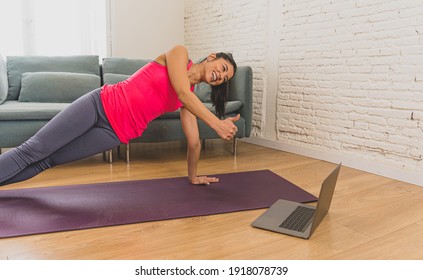 Young Beautiful Latin Woman Working Out At Home Connected To Online Fitness Class On The Computer Laptop. Woman Personal Trainer Coach On Zoom Teaching Exercises In Live Streaming Workout Class.