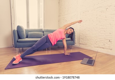 Young Beautiful Latin Woman Working Out At Home Connected To Online Fitness Class On The Computer Laptop. Woman Personal Trainer Coach On Zoom Teaching Exercises In Live Streaming Workout Class.