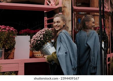 Young beautiful laughing woman holding bouquet of chrysanthemum in pot at florist store against flowers background. Customer, buyer. Saleswoman. Woman florist. Small business. Floral shop. - Shutterstock ID 2394409167