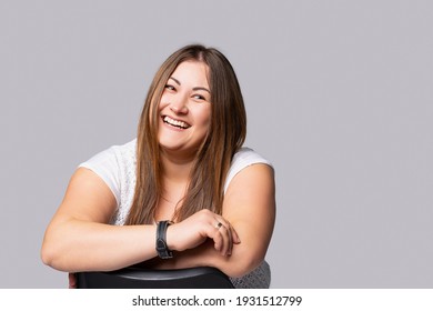 Young Beautiful Long Haired Woman With Natural Makeup On Grey Background Plus Size Model Smiling Cute Looking Into Distance. Portrait Of A Happy And Confident Overweight Model.