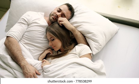 Young beautiful and loving couple kiss and hug into bed while waking up in the morning. Top view of attractive man kissing and talking his smiling wife