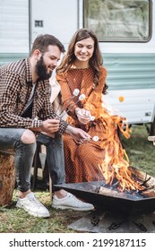 Young Beautiful Loving Couple Travelling Across Country In The Van. Millennial Man And Woman In A Travel Camper. Cozy Atmosphere, Vacations Vibe. Drinking Tea, Cooking Marshmallow On A Campfire