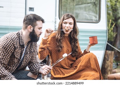 Young Beautiful Loving Couple Travelling Across Country In The Van. Millennial Man And Woman In A Travel Camper. Cozy Atmosphere, Vacations Vibe. Playing Guitar, Drinking Tea, Cooking On A Campfire