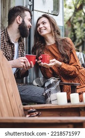 Young Beautiful Loving Couple Travelling Across Country In The Van. Millennial Man And Woman In A Travel Camper. Cozy Atmosphere, Vacations Vibe. Drinking Tea, Cooking Marshmallow On A Campfire