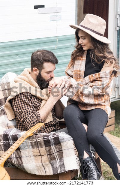 Young beautiful loving couple travelling across\
country in the van. Millennial man and woman in a travel camper.\
Cozy atmosphere, vacations vibe. Playing guitar, drinking tea,\
cooking on a campfire