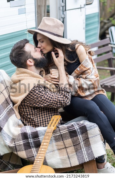 Young beautiful loving couple travelling across\
country in the van. Millennial man and woman in a travel camper.\
Cozy atmosphere, vacations vibe. Playing guitar, drinking tea,\
cooking on a campfire