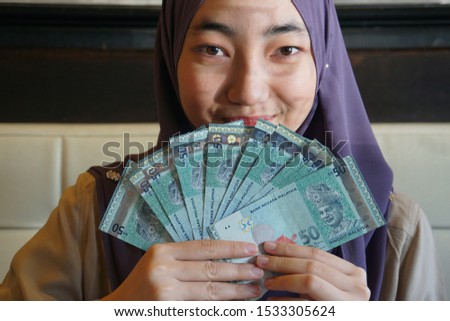 Young Beautiful Malaysian Muslim woman holding Ringgit notes