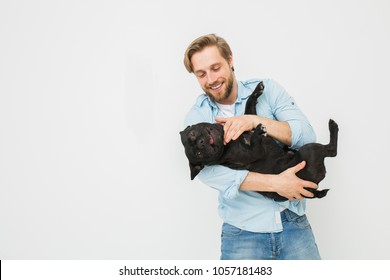 Young And Beautiful Man Holding His Dog In His Arms With Love And Playing With Him, Against A White Background