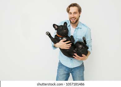 Young And Beautiful Man Holding His Dog In His Arms With Love And Playing With Him, Against A White Background