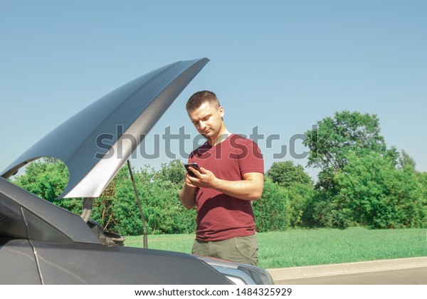 Young and beautiful man near a broken car with an
open hood, talking on the phone. Problems with the machine, does
not start, does not work