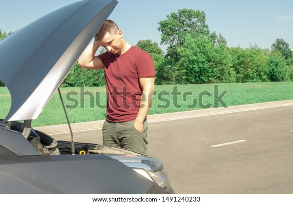 Young and\
beautiful man near a broken car with an open hood. Problems with\
the machine, does not start, does not\
work