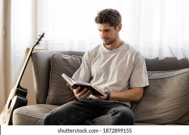 Young Beautiful Man In Reading A Book On A Sofa At Home