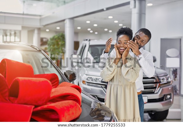 young and beautiful\
married couple in cars showroom, confident black man buy new car as\
a present for his wife