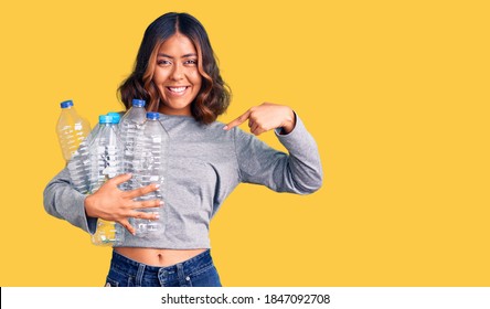 Young Beautiful Mixed Race Woman Holding Recycling Plastic Bottles Pointing Finger To One Self Smiling Happy And Proud 