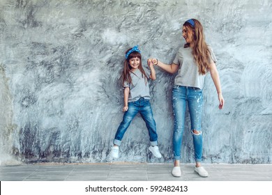 Young Beautiful Mom With Her Daughter Wearing Blank Gray T-shirt And Jeans Posing Against Rough Concrete Wall, Minimalist Street Fashion Style, Family Same Look, Clothing For Parent And Child.