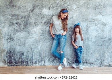 Young Beautiful Mom With Her Daughter Wearing Blank Gray T-shirt And Jeans Posing Against Rough Concrete Wall, Minimalist Street Fashion Style, Family Same Look, Clothing For Parent And Child.