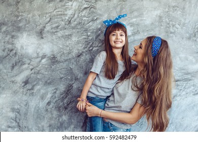 Young Beautiful Mom With Her Daughter Wearing Blank Gray T-shirt And Jeans Posing Against Rough Concrete Wall, Minimalist Street Fashion Style, Family Same Look, Clothing For Parent And Child.