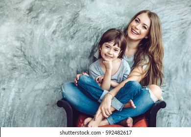 Young Beautiful Mom With Her Daughter Wearing Blank Gray T-shirt And Jeans Posing Against Rough Concrete Wall, Minimalist Street Fashion Style, Family Same Look, Clothing For Parent And Child.