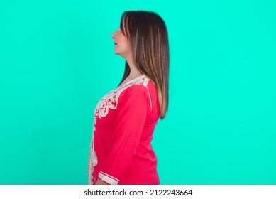 Young Beautiful Moroccan Woman Wearing Traditional Caftan Dress Over Green Background Looking To Side, Relax Profile Pose With Natural Face With Confident Smile.