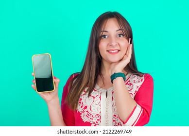 Young Beautiful Moroccan Woman Wearing Traditional Caftan Dress Over Green Background Hold Hand Modern Technology Use Touch Face Palm Astonished Impressed Scream Wow Omg Unbelievable Unexpected