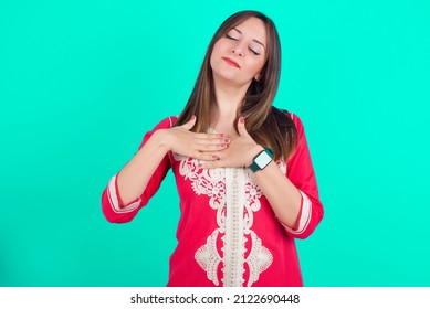 Young Beautiful Moroccan Woman Wearing Traditional Caftan Dress Over Green Background Smiling With Hands On Chest With Closed Eyes And Grateful Gesture On Face. Health Concept.