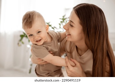 a young beautiful mother with a baby boy hugging on the bed at home in the bedroom, mother's care and love, portrait of a happy mother with a child, healthy motherhood