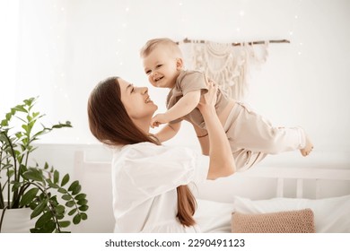 a young beautiful mother with a baby boy hugging on the bed at home in the bedroom, mother's care and love, portrait of a happy mother with a child, healthy motherhood - Powered by Shutterstock