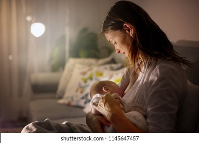 Madre joven, amamantando a su bebé recién nacido de noche, luz tenue. Madre lactante