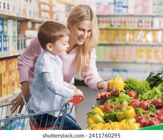 Young beautiful mother buying groceries with her son at the supermarket, they are picking healthy fresh vegetables in the produce section - Powered by Shutterstock