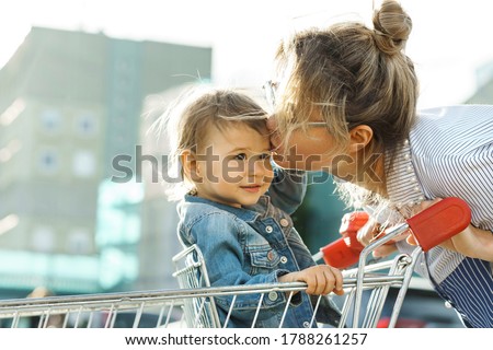 Young beautiful mother and her cute little son in a shopping cart  beside a supermarket