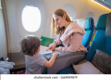  Young Beautiful Mother Sits In An Airplane Chair Shows With Finger A Page In A Book To Her Little Cute Toddler, Who Is Standing In Front Of Her. Close-up, Soft Focus, Top View. Copy Space,blank Page