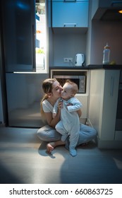 Young Beautiful Mother Sitting With Her Baby Son On Kitchen Floor At Late Night