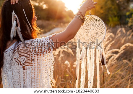 Young Beautiful And Mysterious Woman Holding Dreamcatcher In field. 