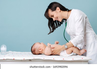 A young beautiful pediatrician examines the baby in a diaper and smiles at him. Isolated not blue background