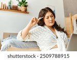 A young, beautiful plus size woman thoughtfully interacts with her laptop while relaxing at home.