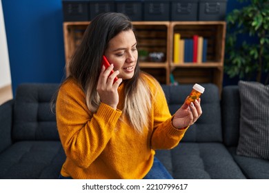 Young beautiful plus size woman talking on smartphone holding pills at home - Powered by Shutterstock