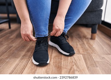 Young beautiful plus size woman tying shoe at home - Powered by Shutterstock