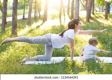 Young beautiful pregnant mother with baby son exercising and doing yoga on blue mat at summer park at sunset. Sportive and healthy motherhood. Fitness, happy maternity and healthy lifestyle concept. - Powered by Shutterstock