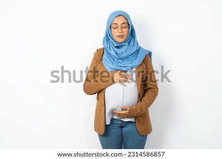 Young beautiful pregnant muslim woman wearing hijab over white studio background nice-looking sweet charming cute attractive lovely winsome sweet peaceful closed eyes